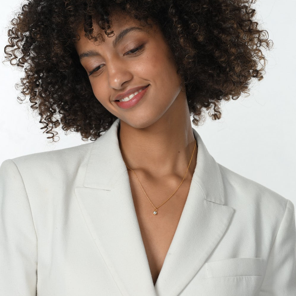 Frau im weißen Blazer trägt eine Halskette mit einem goldenen Anhänger mit einem Labordiamanten im runden Brillantschliff.