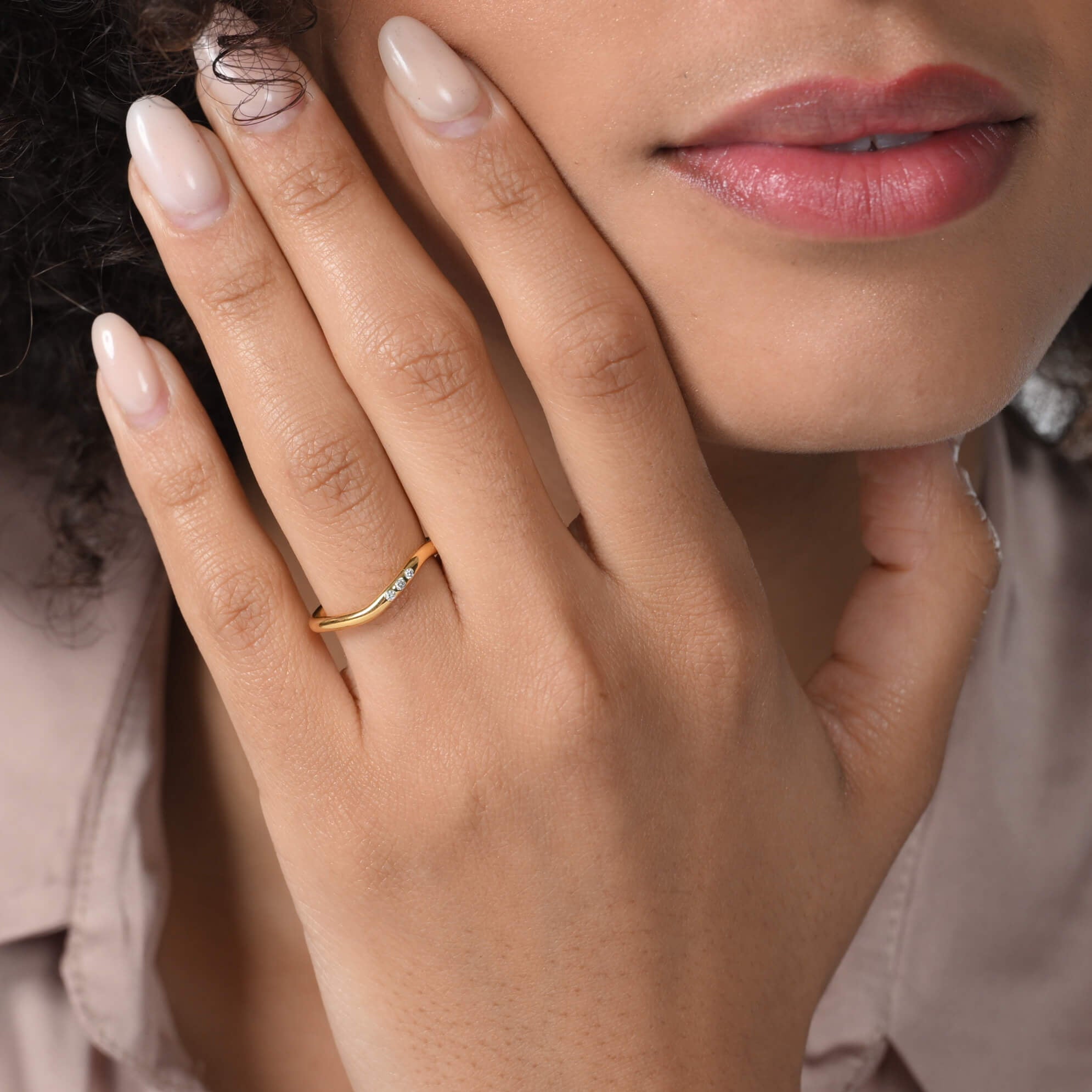 Nahaufnahme von einem zierlichen vergoldeten Ring mit drei runden Labordiamanten im Brillantschliff am Ringfinger getragen.
