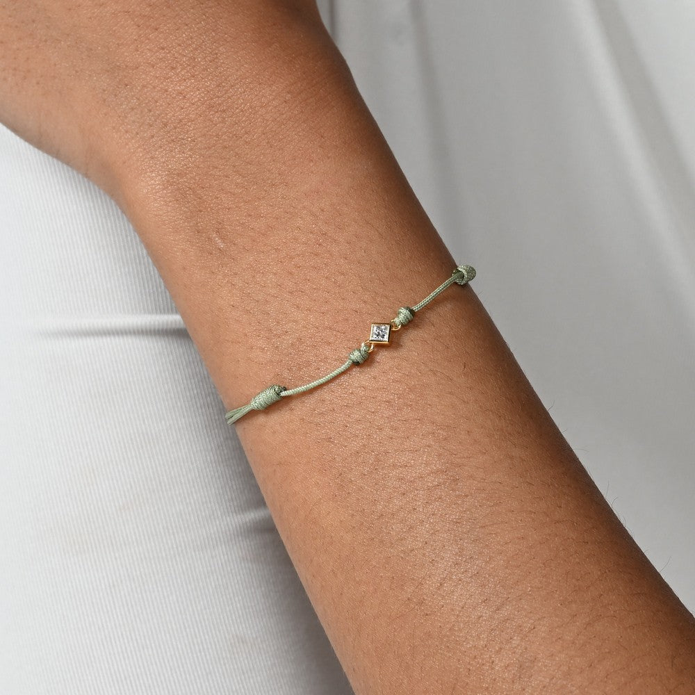 Nahaufnahme von einem grünen Cord-Armband mit einem kleinen Labordiamanten im Princessschliff am Arm getragen.
