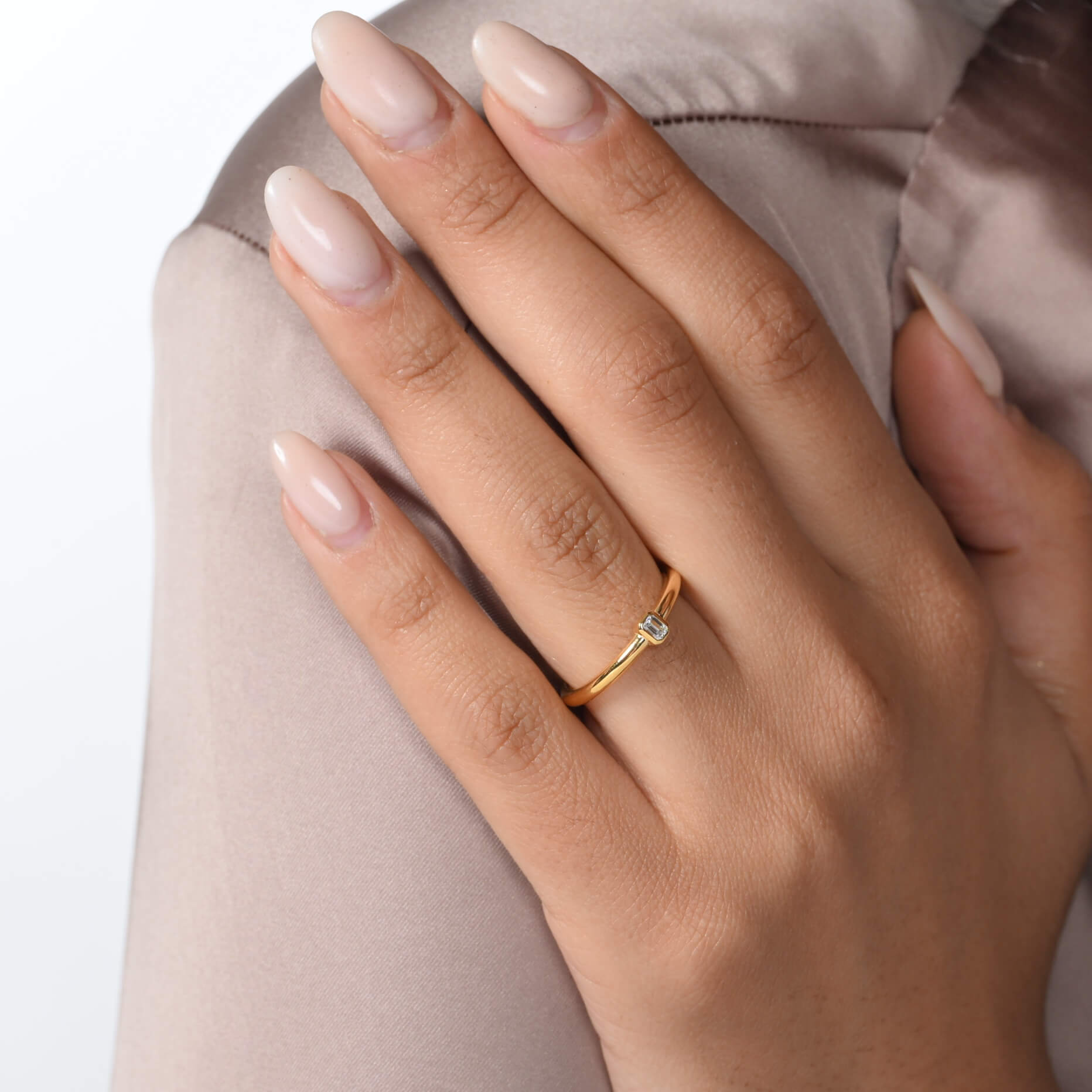 Nahaufnahme von einem vergoldeten Verlobungsring mit einem Labordiamanten im Smaragdschliff am Ringfinger getragen.