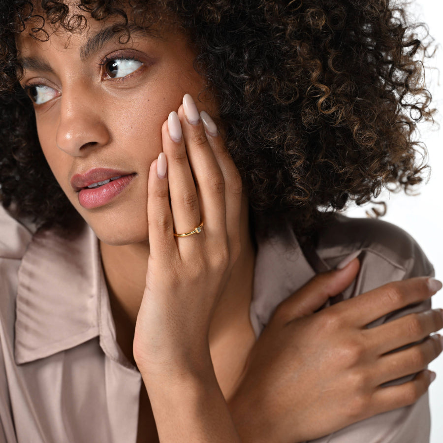 Frau trägt einen einen vergoldeten Verlobungsring mit einem Labordiamanten im Smaragdschliff in Zargenfassung am Ringfinger.