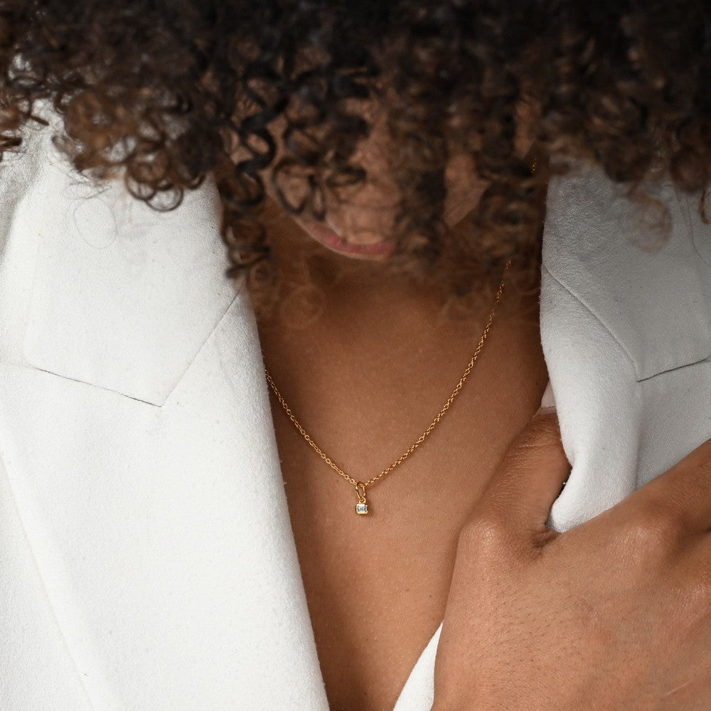 Frau im weißen Blazer trägt eine Halskette mit einem goldenen Anhänger mit kleinem Labordiamanten in Oktagonform.