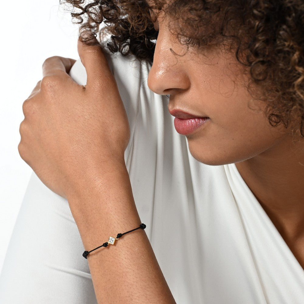 Nahaufnahme von einem schwarzen Cord-Armband mit einem Labordiamanten im Princessschliff am Arm getragen.