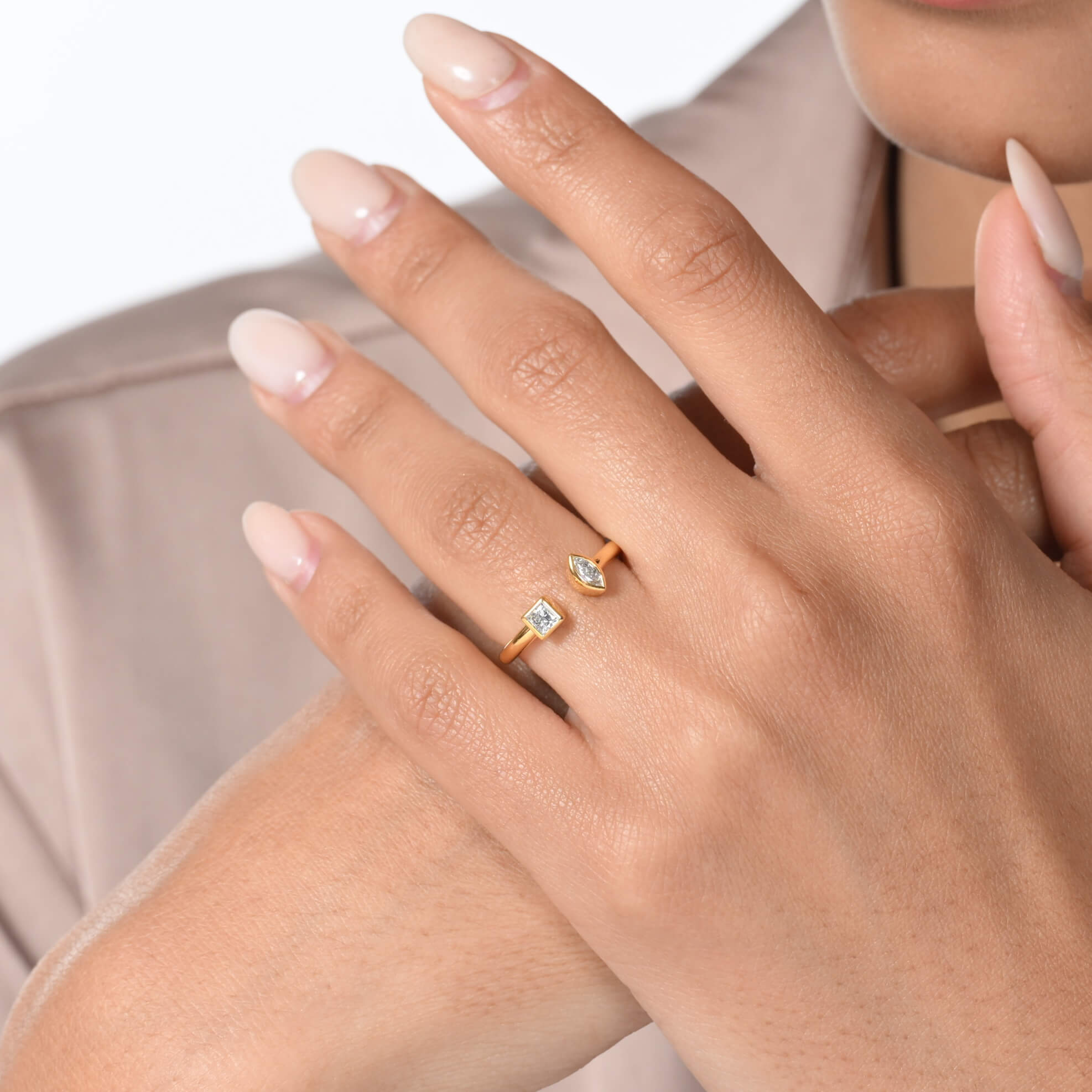 Nahaufnahme von einem vergoldeten Ring mit zwei Labordiamanten im Carree- und im Marquiseschliff am Ringfinger getragen.