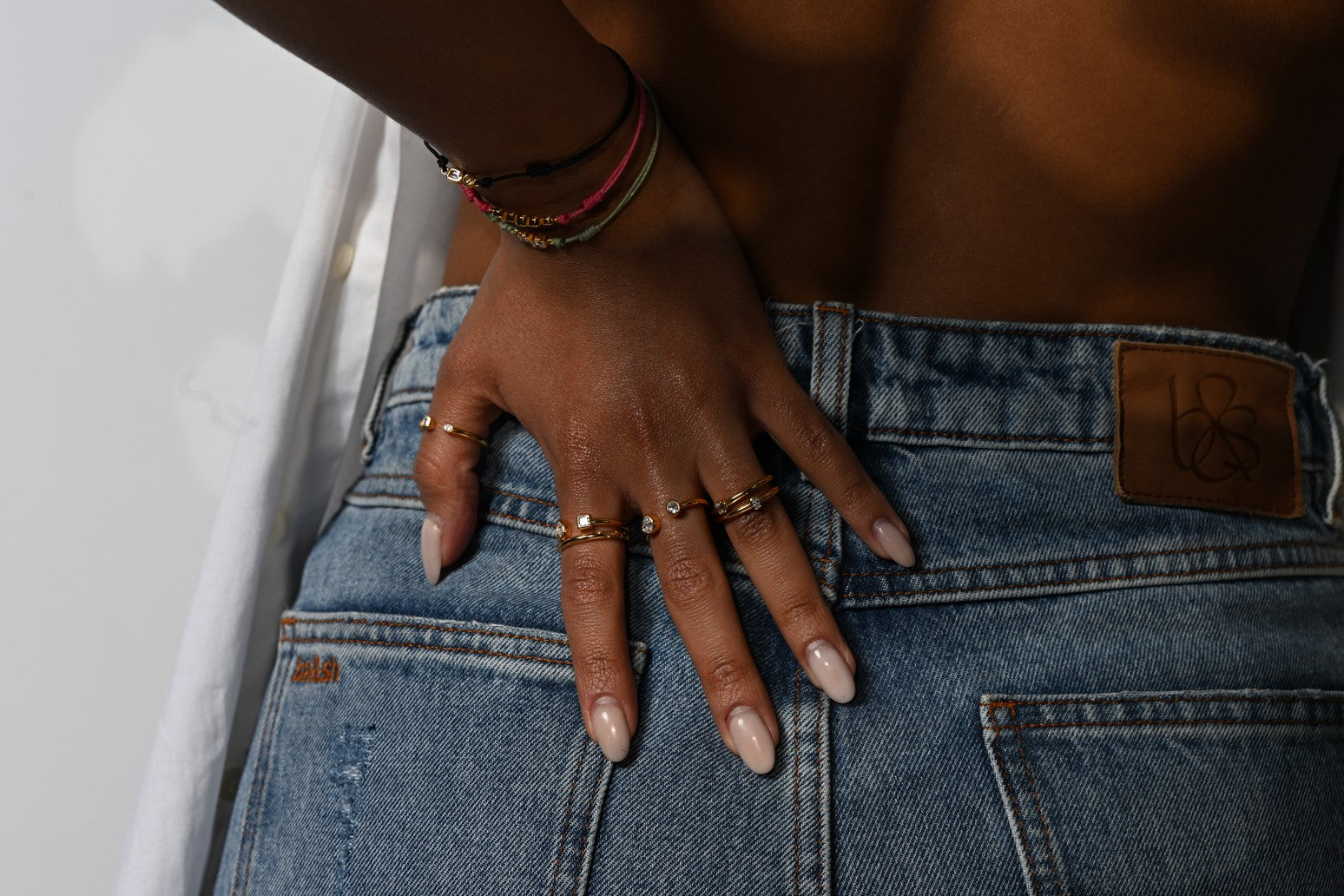 Model trägt einen Ring-Stack und mehrere Cord-Armbänder mit Lab-Grown-Diamanten. Die Hand ruht lässig auf einer Jeans.
