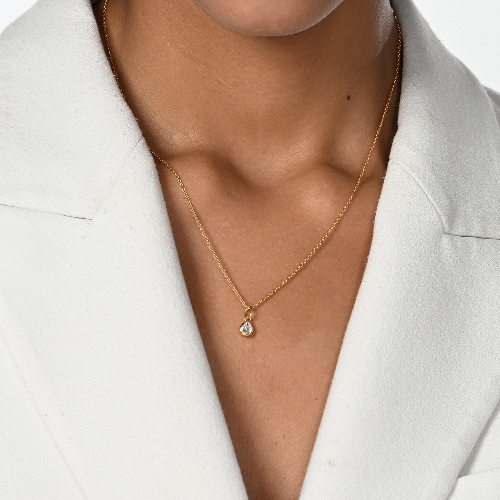 Frau im weißen Blazer trägt eine Halskette mit einem goldenen Anhänger mit einem Labordiamanten in Tropfenform.