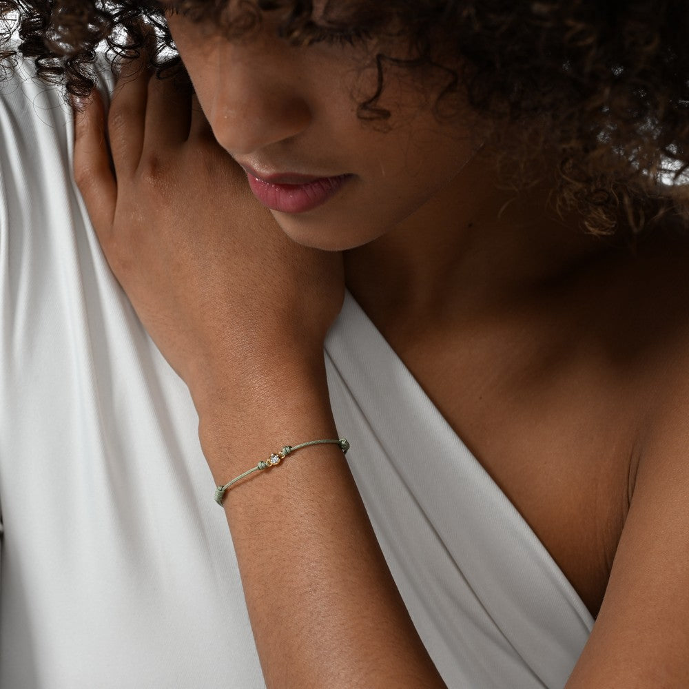 Frau trägt eine grünes Cord-Armband mit einem Labordiamanten im Brillantschliff in Zargenfassung. 