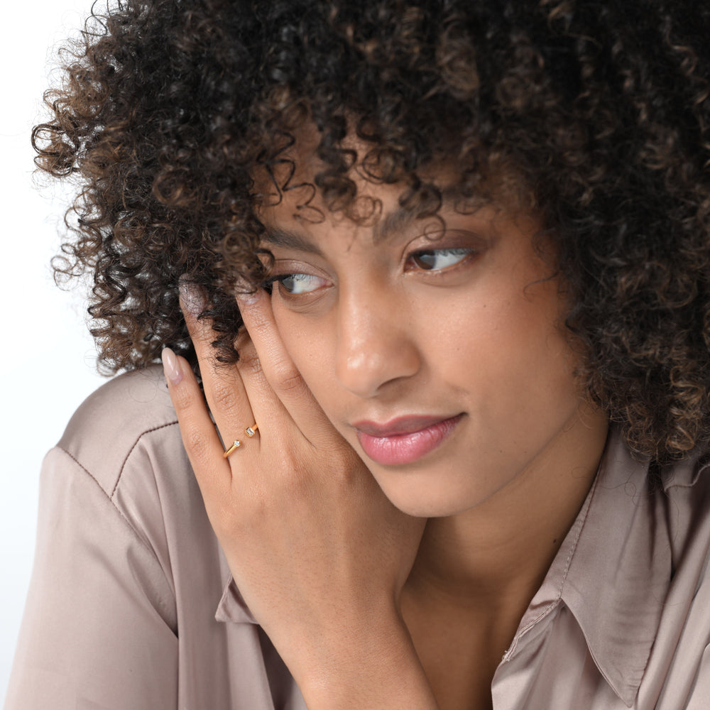 Frau trägt einen vergoldeten Ring mit 2 Labordiamanten im Smaragd- und im Brilliantschliff in Zargenfassung am Ringfinger.  