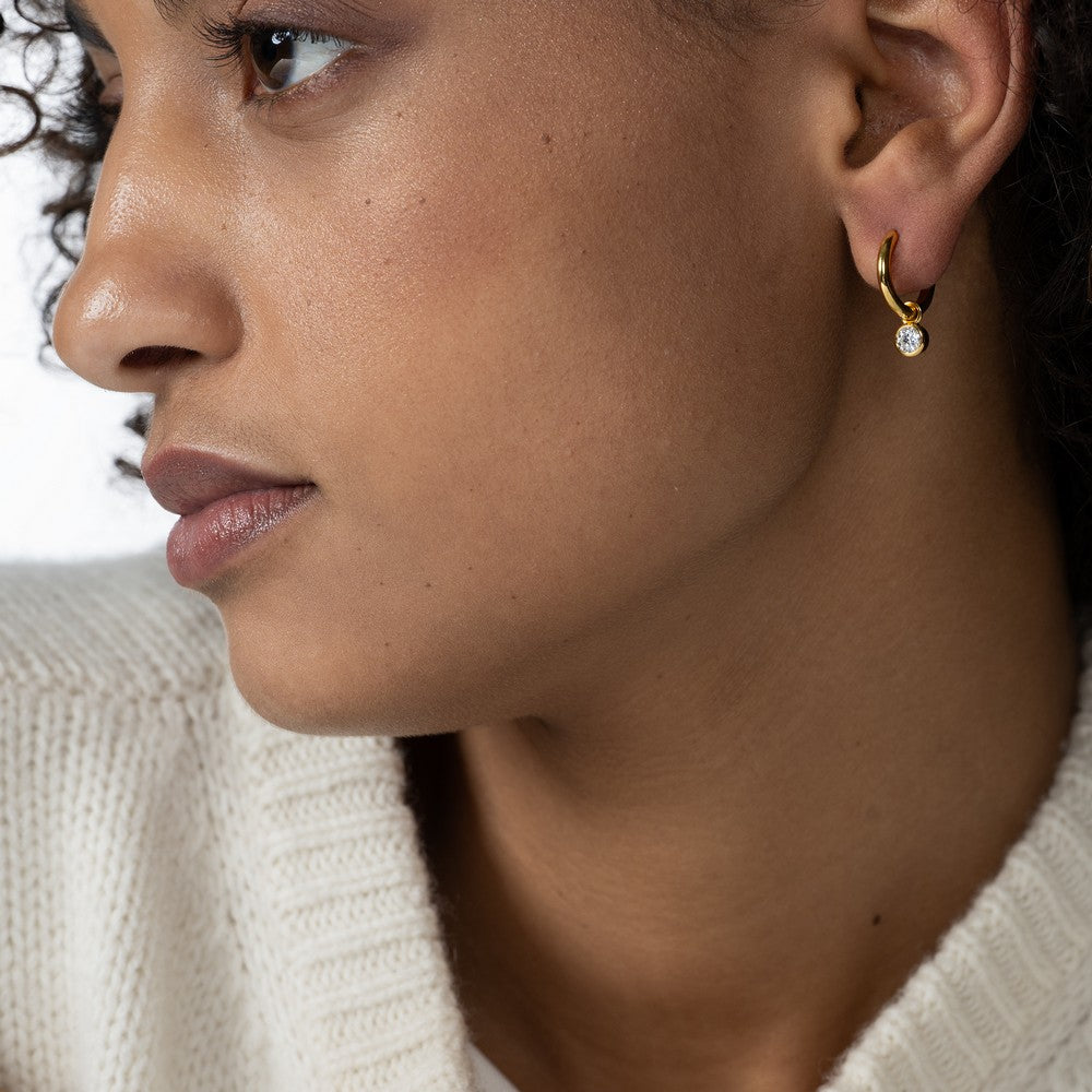 Seitensicht von einer Frau mit lockigen Haaren mit einem Diamant-Charm mit einem Labordiamanten im runden Brillantschliff im Ohr.
