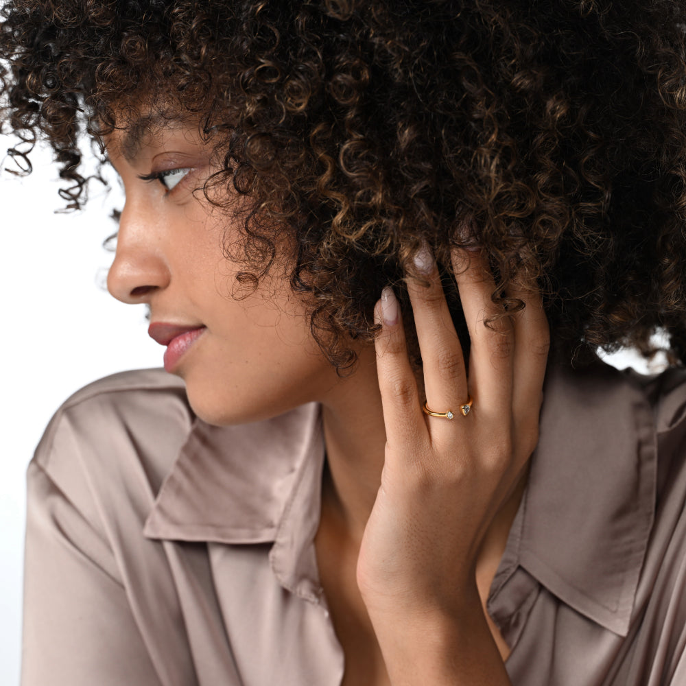 Frau trägt einen vergoldeten Ring mit zwei Labordiamanten im Tropfenschliff und im Ovalschliff in Zargenfassung am Ringfinger.  