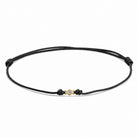 Detailansicht von einem schwarzen Cord-Armband mit einem kleinen Labordiamanten im Brillantschliff  in Zargenfassung auf weißem Hintergrund.