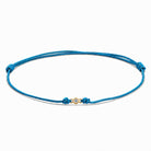 Detailansicht von einem blauen Cord-Armband mit einem kleinen Labordiamanten im Brillantschliff  in Zargenfassung auf weißem Hintergrund.