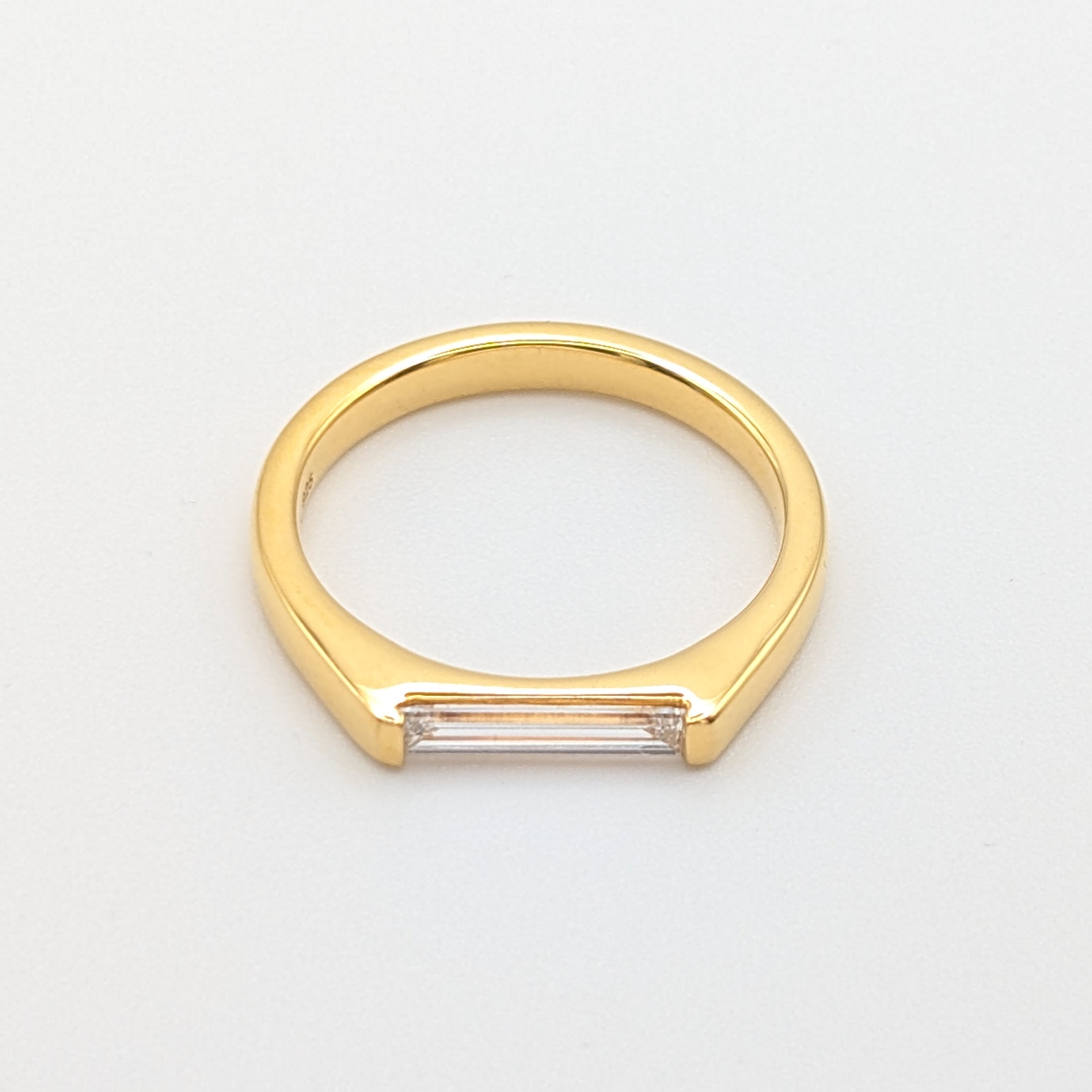 Eing goldfarbener Ring mit einem länglichen Lab-Grown Diamanten im Baguetteschliff.